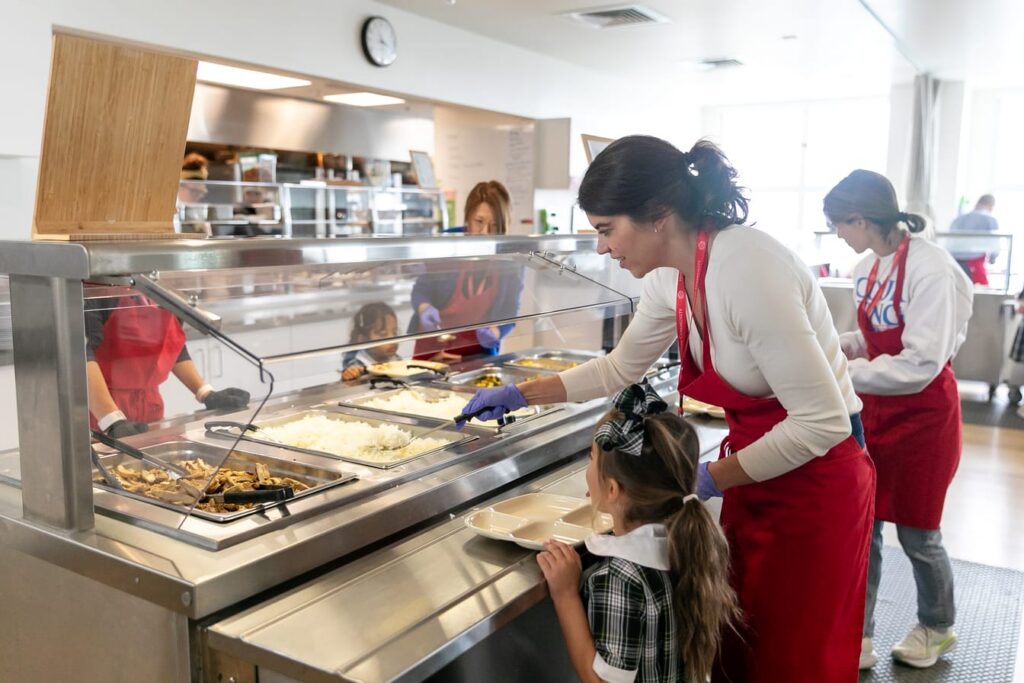 Parent volunteer serving lunch to a young student