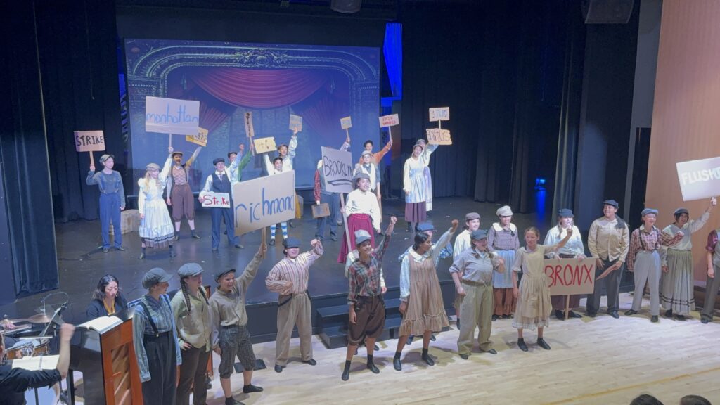 Students holding protest signs on state in a performance of Newsies